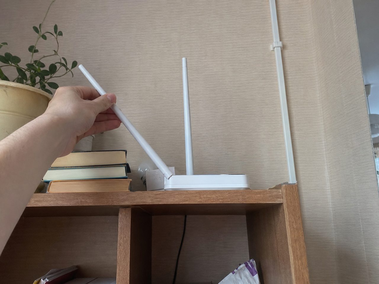 Рука наклоняет антенну роутера на верхней полке стеллажа