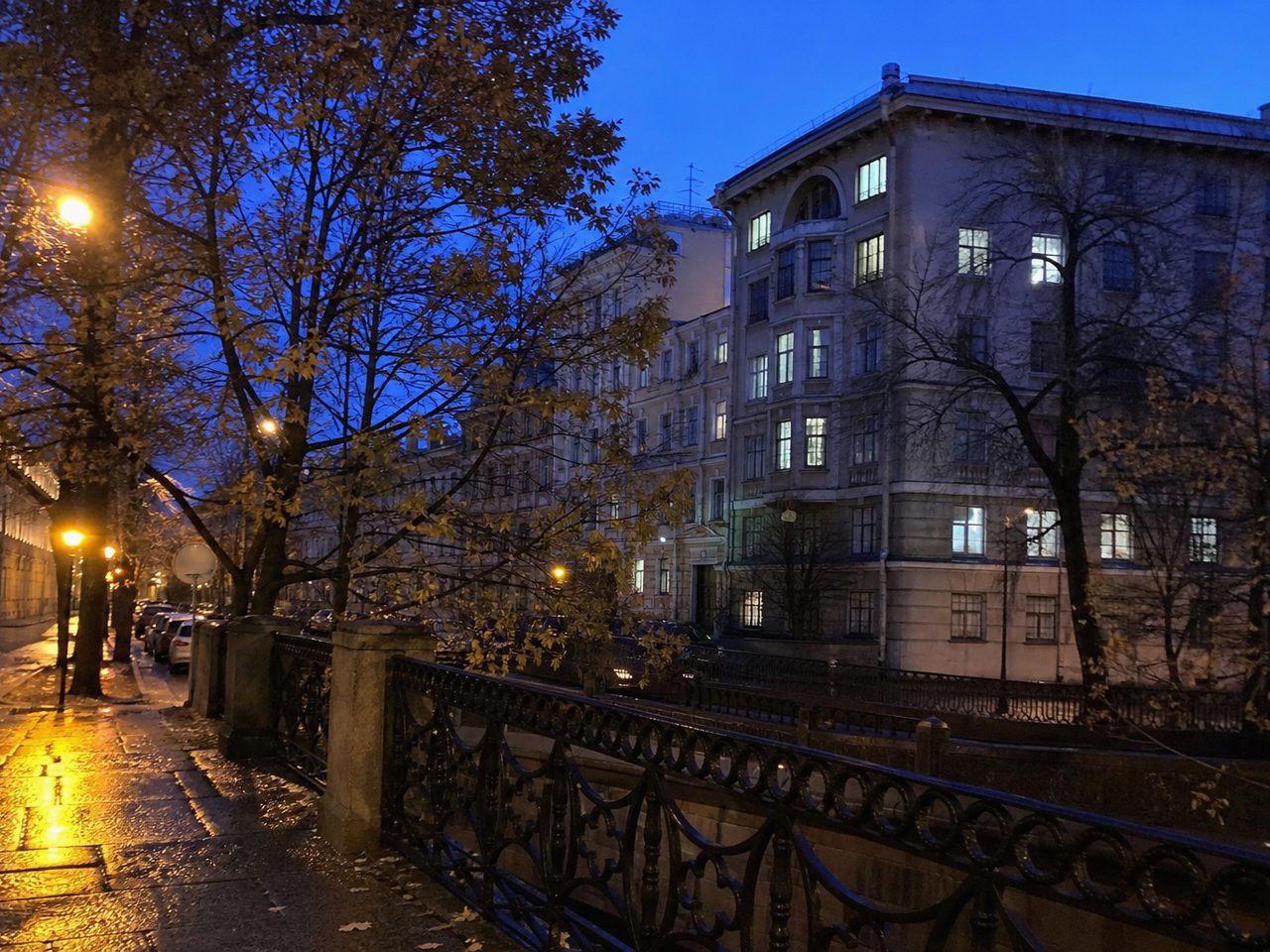Вечерняя улица после дождя: тёмно-синее небо и оранжевые фонари, отражённые в мокрой брусчатке