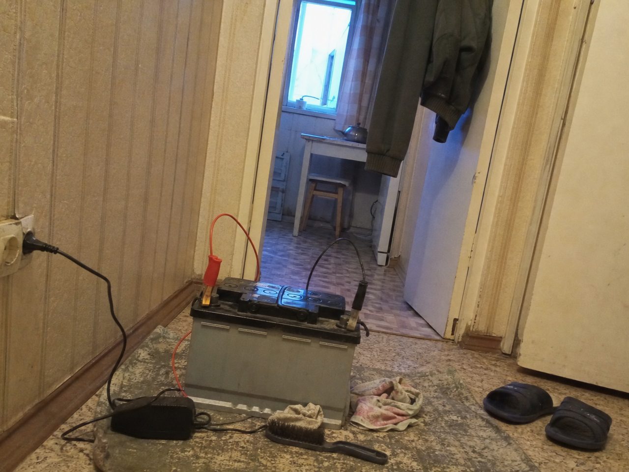 Автомобильный аккумулятор на зарядке на полу в прихожей