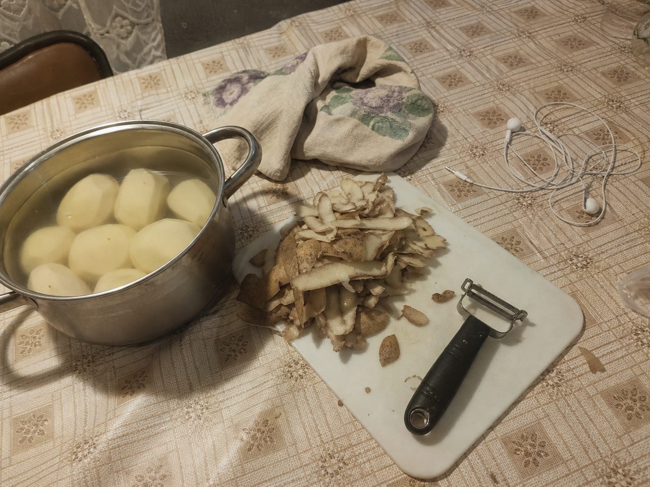 Кухонный стол с почищенной картошкой, очистками и проводными наушниками