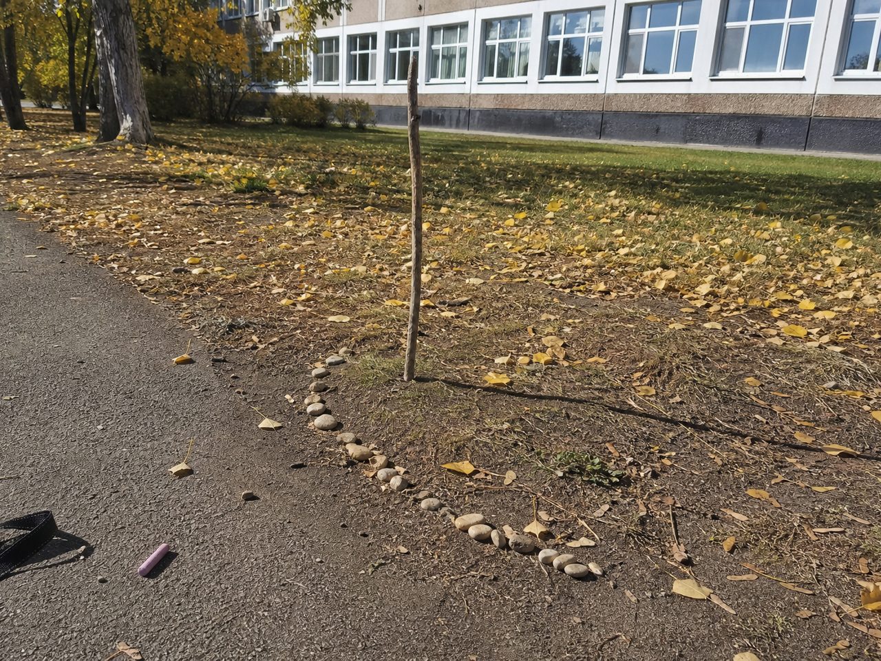 Палка во дворе школы, её тень и ряд камешков, отмечающих конец тени