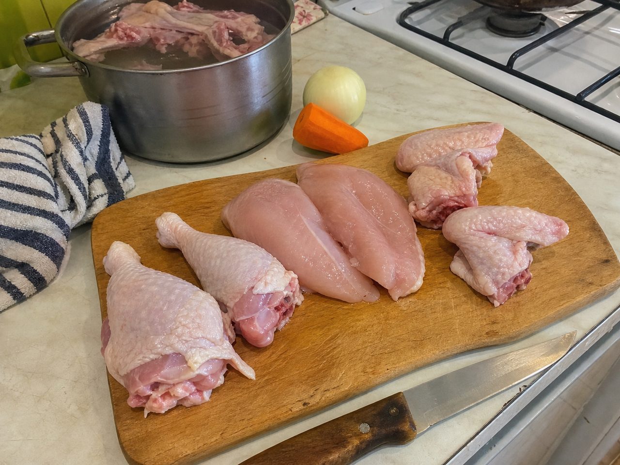 Разделанная курица на доске: грудка, ножки и крылья, спинка с шеей в кастрюле с водой