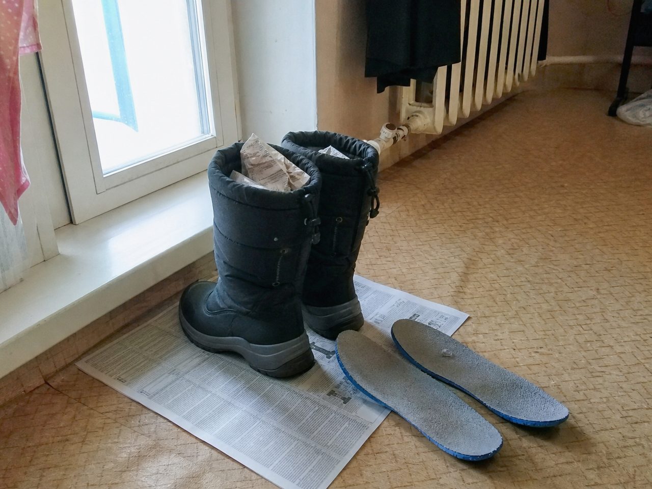 Пара зимних ботинок на газете у окна с бумагой внутри, рядом вынутые стельки